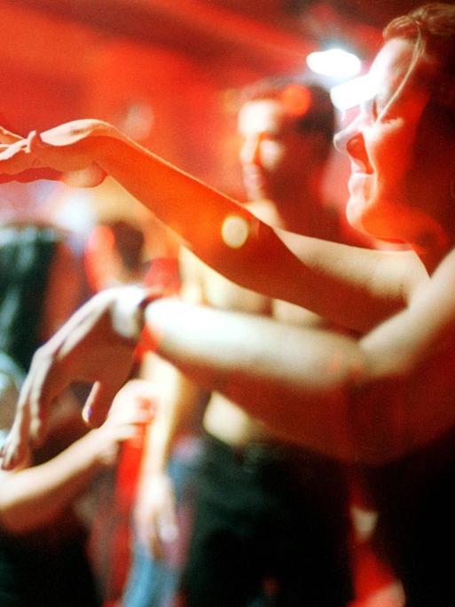 Ekstatisch tanzende Clubgänger im Berliner Club Tresor. Im Vordergrund rechts tanzt ein Mensch mit geschlossenen Augen und bewegt die Hände vor sich zur Musik.