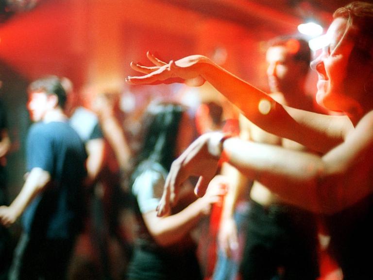 Ekstatisch tanzende Clubgänger im Berliner Club Tresor. Im Vordergrund rechts tanzt ein Mensch mit geschlossenen Augen und bewegt die Hände vor sich zur Musik.