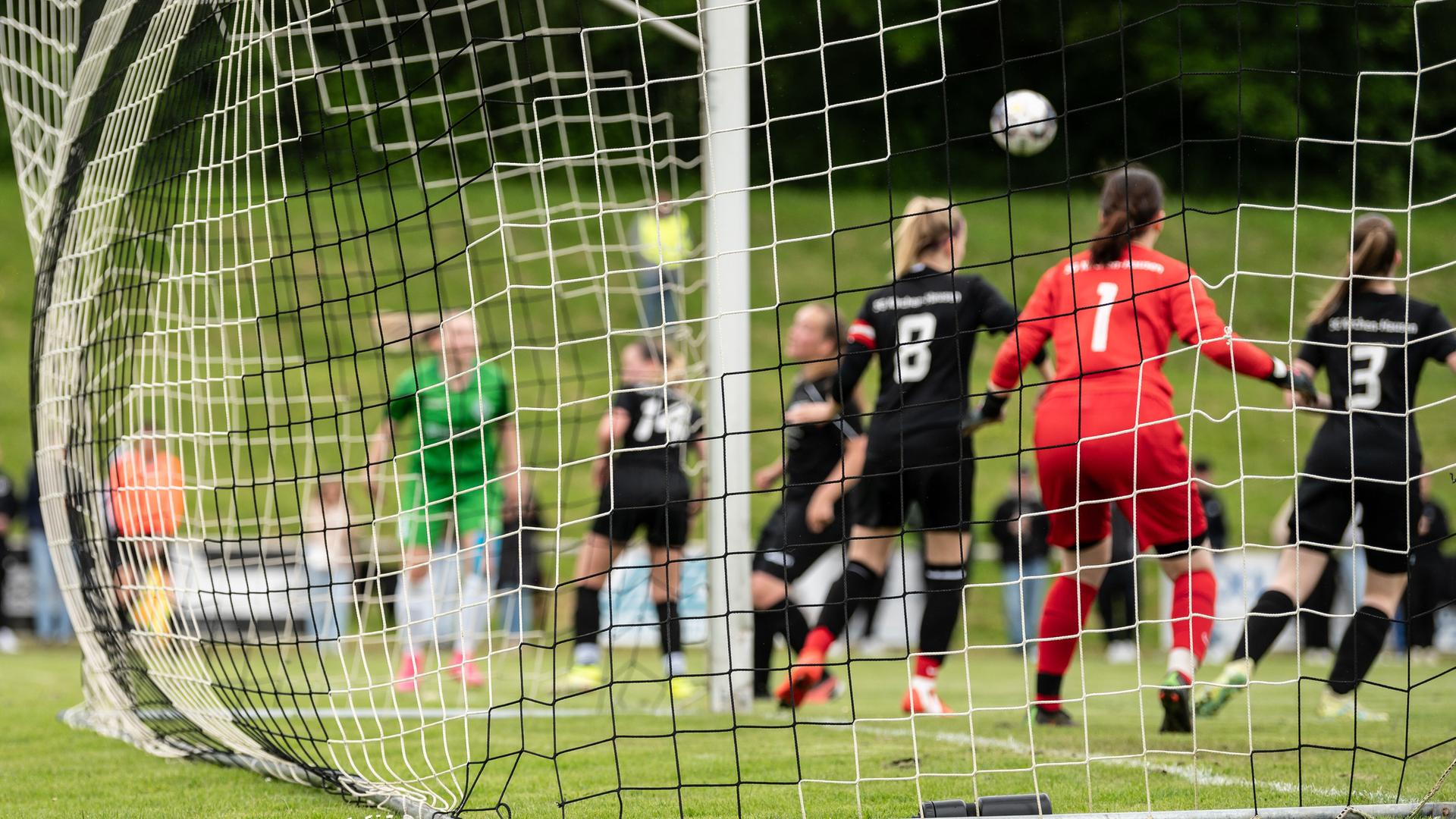 Spielerinnen sind während eines Fußballspiels hinter einem Netz eines Tors zu sehen.