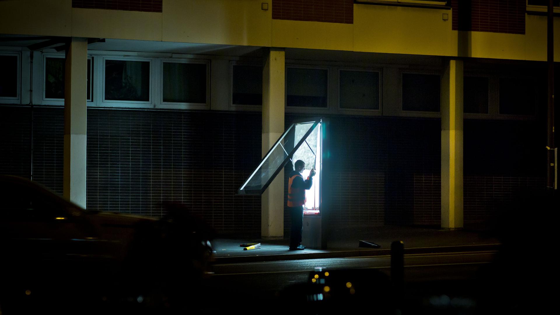 Ein Mann wechselt nach Einbruch der Dunkelheit in Frankfurt am Main (Hessen) Plakate, die von hinten durch Neonröhren beleuchtet werden.