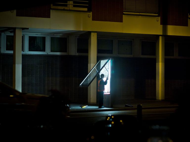 Ein Mann wechselt nach Einbruch der Dunkelheit in Frankfurt am Main (Hessen) Plakate, die von hinten durch Neonröhren beleuchtet werden.