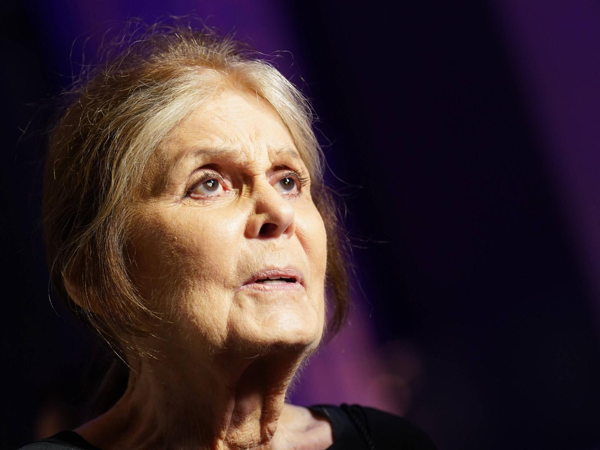 Porträt von Gloria Steinem vor dunklem Hintergrund. Sie schaut mit weit geöffnet Augen nach rechts oben. Porträt von Gloria Steinem vor dunklem Hintergrund. Sie schaut mit weit geöffnet Augen nach rechts oben.