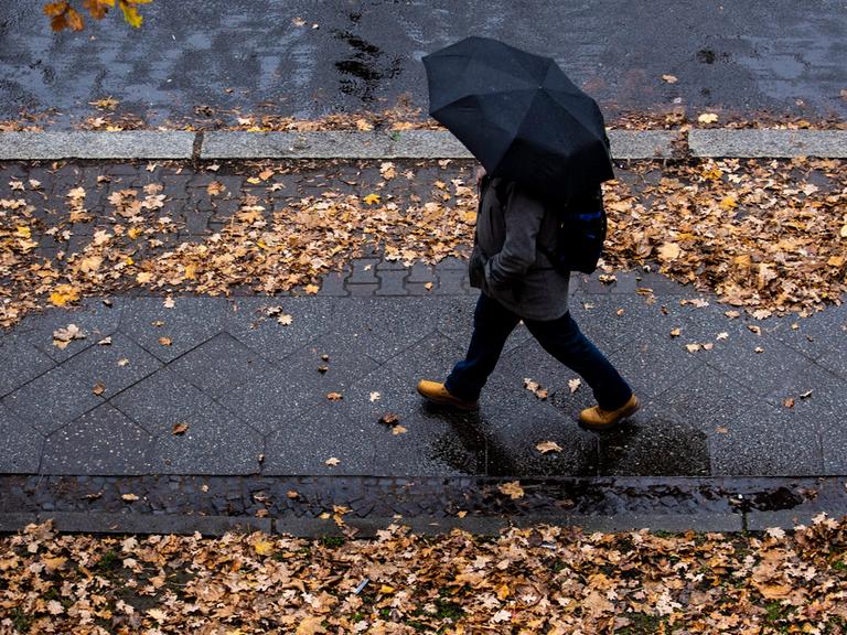 Ein Mensch läuft mit dunklem Regenschirm durch den Regen.