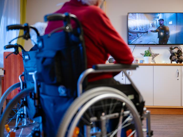 Bewohner eines Senioren- und Pflegezentrums sitzen im Aufenthaltsraum und schauen Fernsehen. 