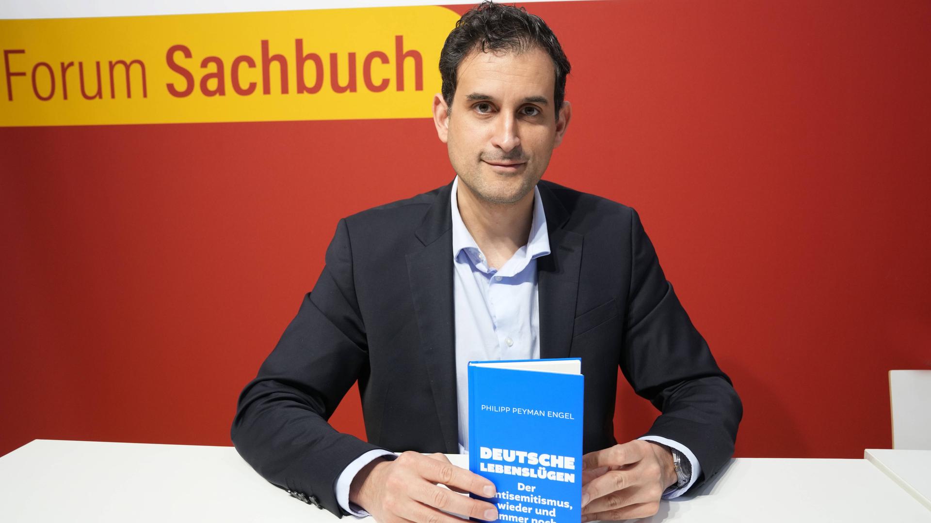 Philipp Peymann Engel sitzt an einem Tisch und zeigt sein Buch "Deutsche Lebenslügen". Philipp Peymann Engel sitzt an einem Tisch und zeigt sein Buch "Deutsche Lebenslügen".