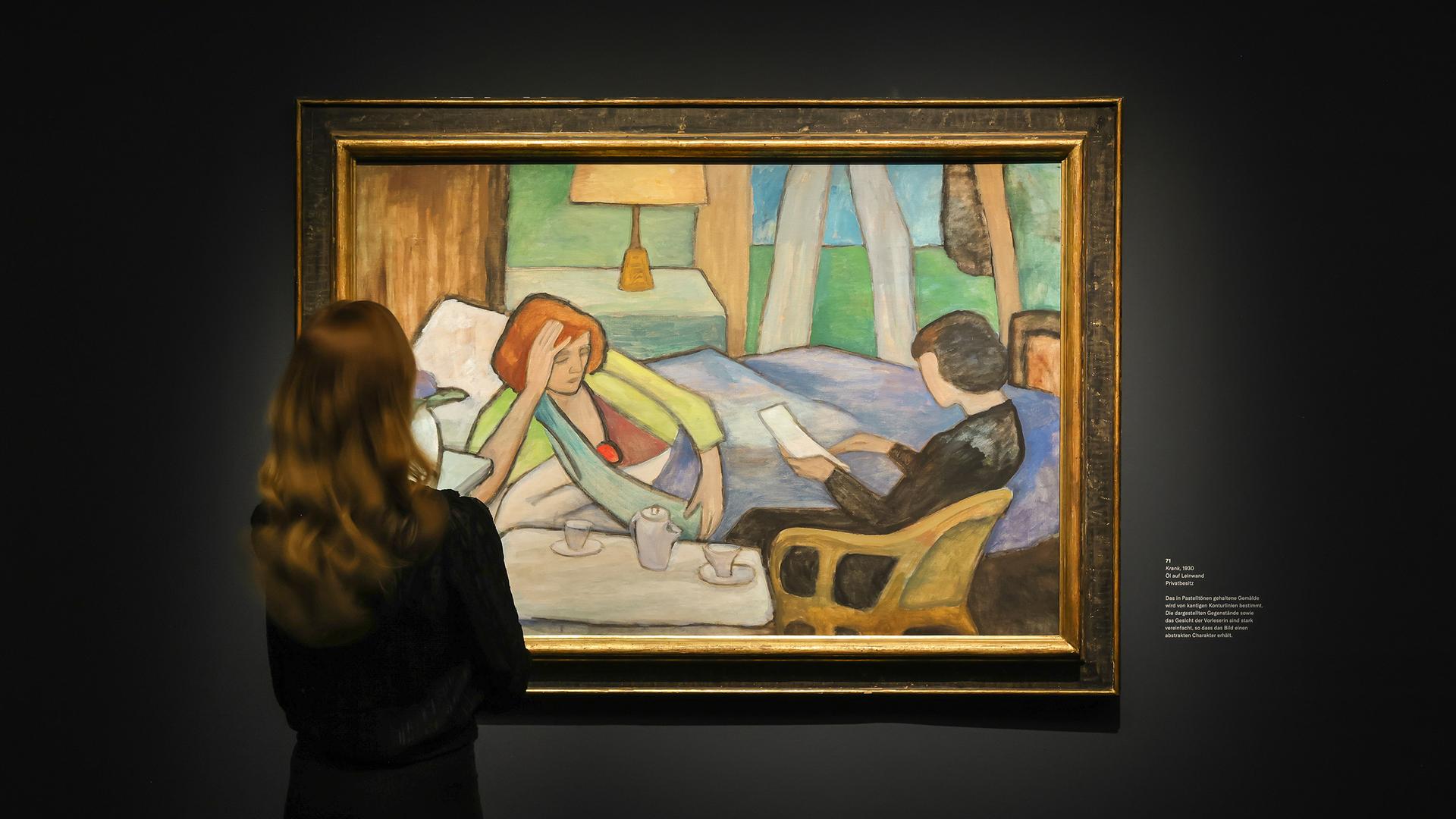 Eine Frau schaut sich ein Gemälde von Gabriele Münter in der Ausstellung "Menschenbilder" im Bucerius Kunst Forum in Hamburg an. Das Gemälde zeigt eine Frau, die halb unter Decken liegt und sich mit der rechten Hand hochstützt, sodass ihr Oberkörper seitlich aufgerichtet ist. Eine andere Frau liest in einem Brief.