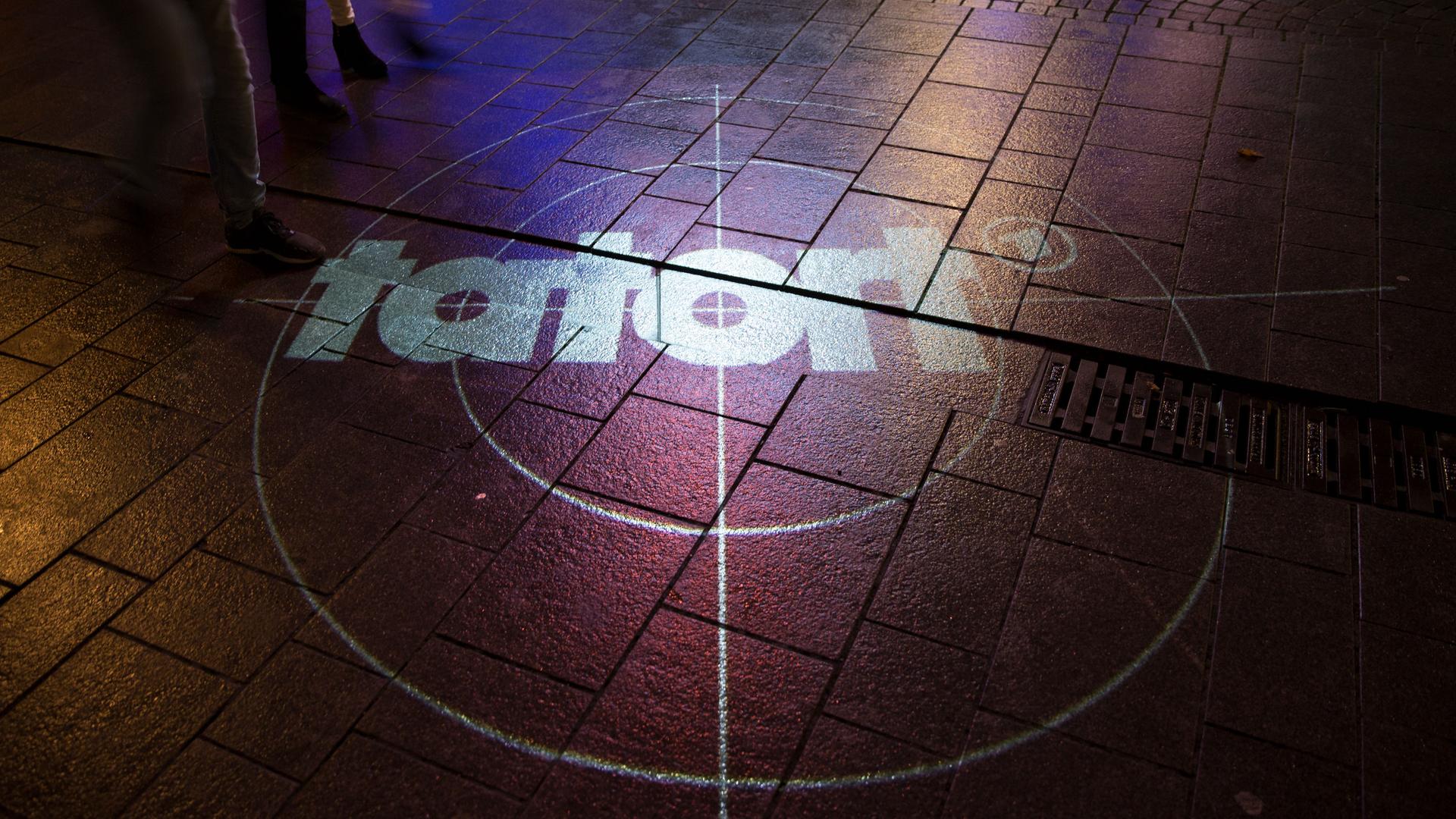 Das Logo des ARD Tatorts wird auf eine Straße projiziiert, wo Menschen laufen. Foto: Noah Wedel/Kirchner-Media