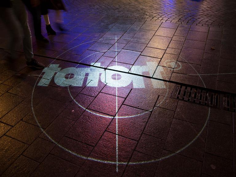 Das Logo des ARD Tatorts wird auf eine Straße projiziiert, wo Menschen laufen. Foto: Noah Wedel/Kirchner-Media