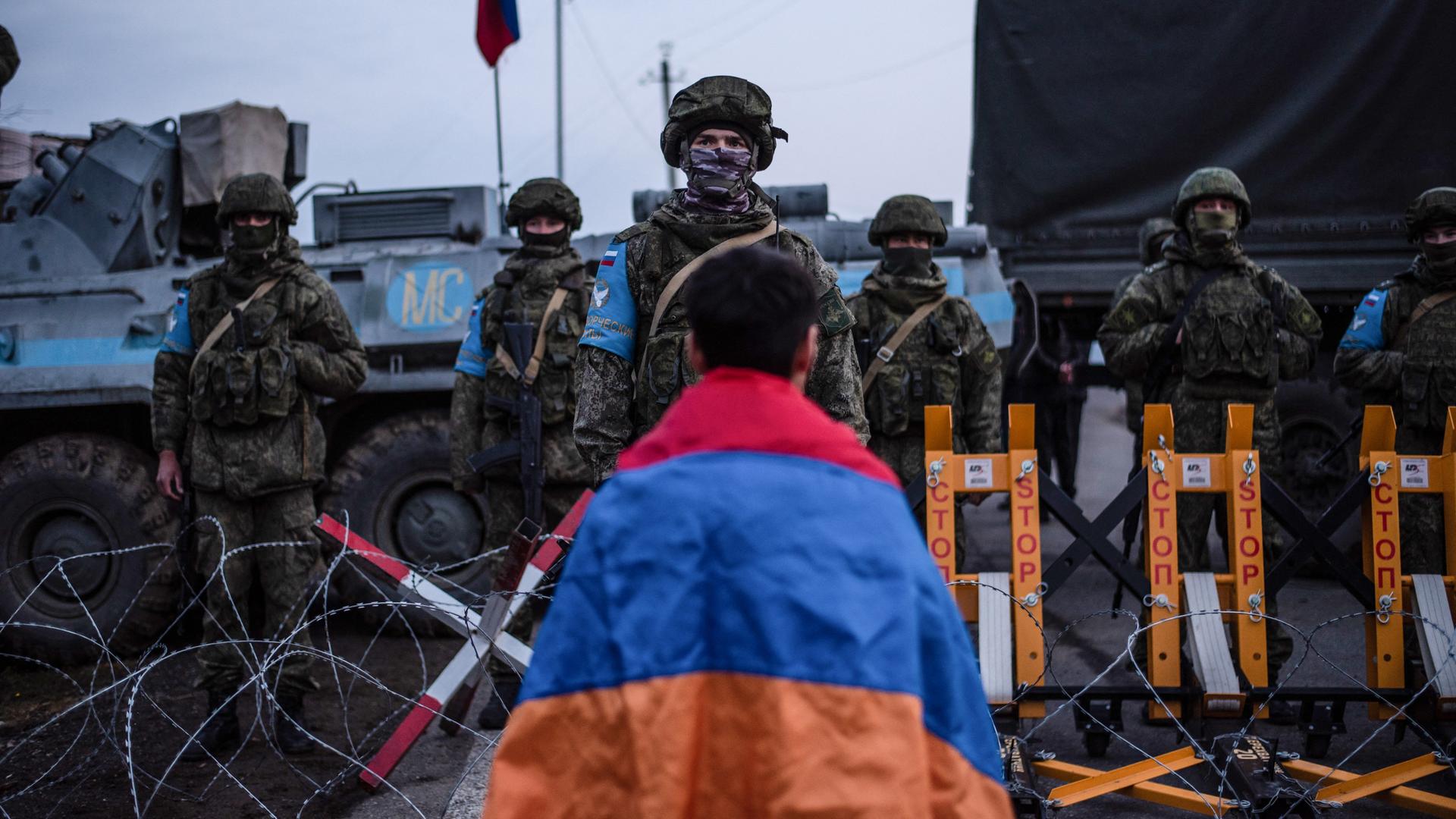 Ein Demonstrant steht in eine armenische Flagge gewickelt vor russischen Soldaten, die eine Straße blockieren.