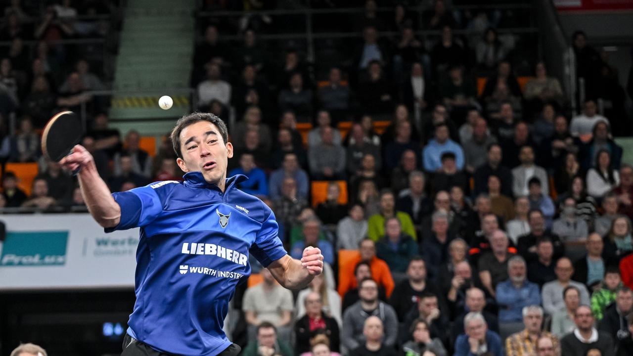 Ein Tischtennisspieler bei einem Schmetterschlag, im Hintergrund ist eine Tribüne mit Zuschauern.