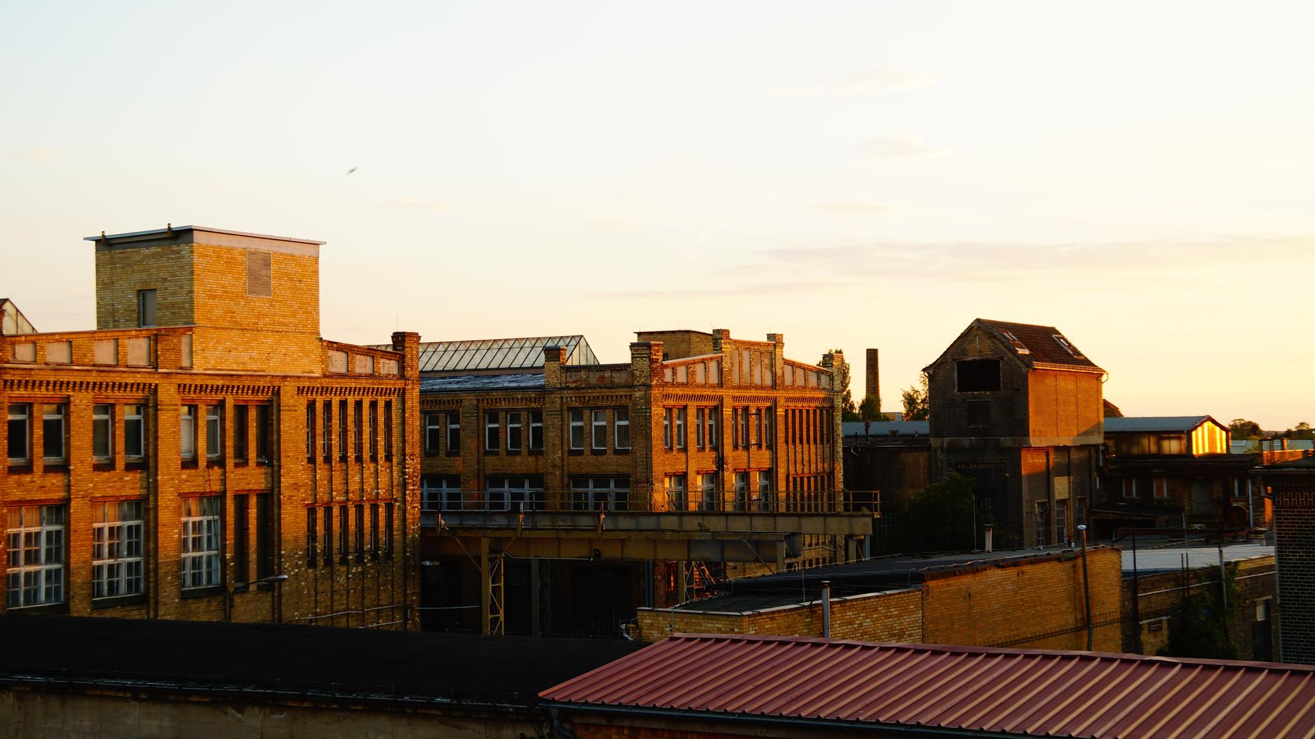 Ein großes, altes Fabrikgebäude  aus dunkelrotem Ziegelstein in der Abendsonne.
