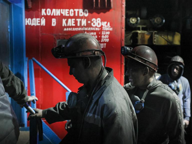 Russische Minenarbeiter gehen in Arbeitskleidung und bedeckt mit schwarzem Kohlestaub vorbei am Tor der Kohlemine Dolzhanskaya-Kapitalnaya im von Russland kontrollierten Luhansk-Gebiet in der Osktukraine.