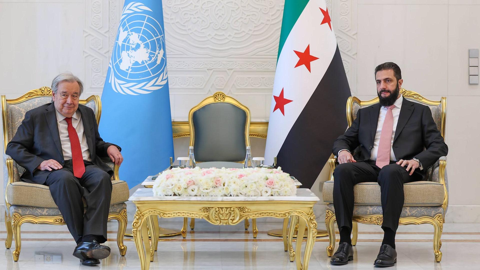 UNO-Generalsekretär Guterres und der syrische Übergangspräsident al-Scharaa sitzen auf zwei großen Stühlen nebeneinander, mit einigem Abstand zwischen ihnen. Hinter ihnen stehen die Flaggen der Vereinten Nationen und Syriens. UNO-Generalsekretär Guterres und der syrische Übergangspräsident al-Scharaa sitzen auf zwei großen Stühlen nebeneinander, mit einigem Abstand zwischen ihnen. Hinter ihnen stehen die Flaggen der Vereinten Nationen und Syriens.