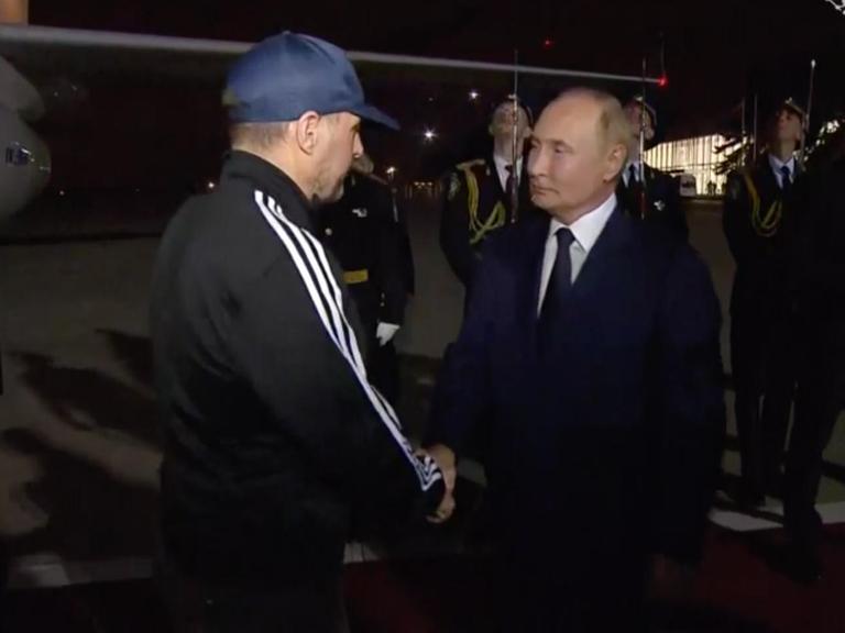 Wladmir Putin begrüßt auf dem nächtlichen Moskauer Flughafen einen Mann im Trainingsanzug mit Basecap per Handschlag.