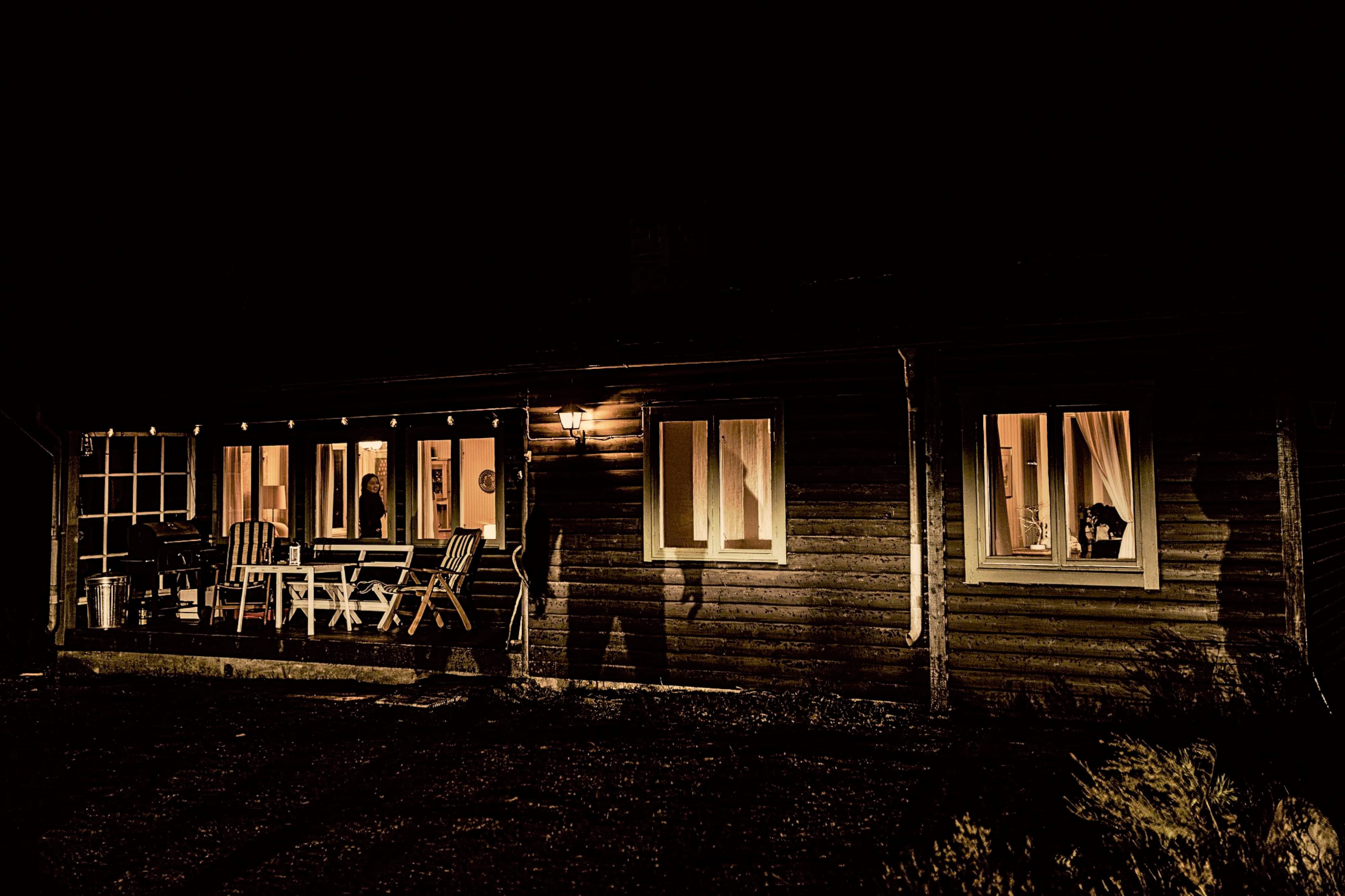 Es ist Nacht, im Holzhaus brennt Licht, auf der Fassade sieht man den großen Schatten eines Mannes.