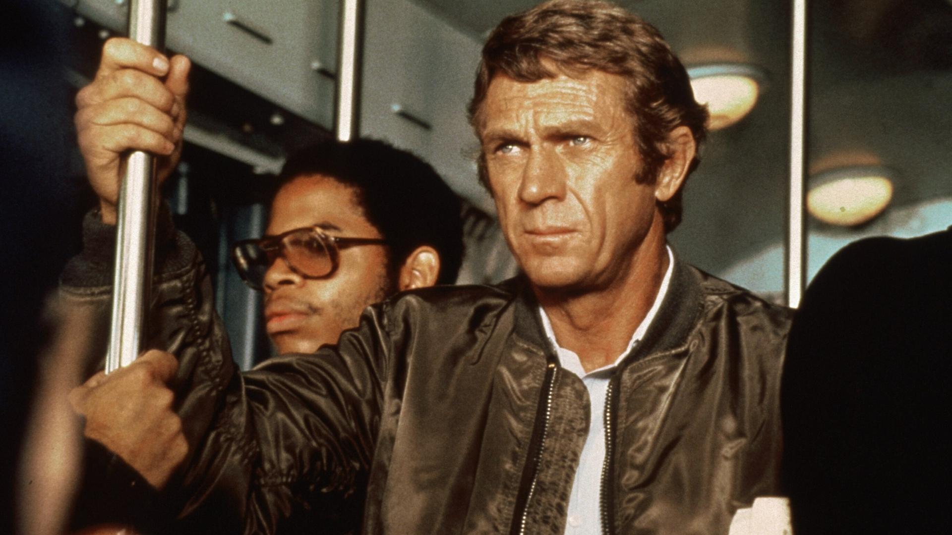 Ein Filmauschnitt mit Steve McQueen aus "The Hunter" Er steht in einem Bus und hält sich an einer Stange fest mit konzentriertem Blick in die Ferne. Ein Filmauschnitt mit Steve McQueen aus "The Hunter" Er steht in einem Bus und hält sich an einer Stange fest mit konzentriertem Blick in die Ferne.