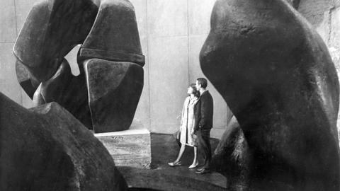 Historisches Schwarzweißfoto eines jungen Paares, das Steinskulpturen in einer Halle betrachtet.