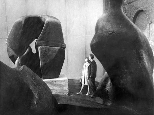 Historisches Schwarzweißfoto eines jungen Paares, das Steinskulpturen in einer Halle betrachtet.