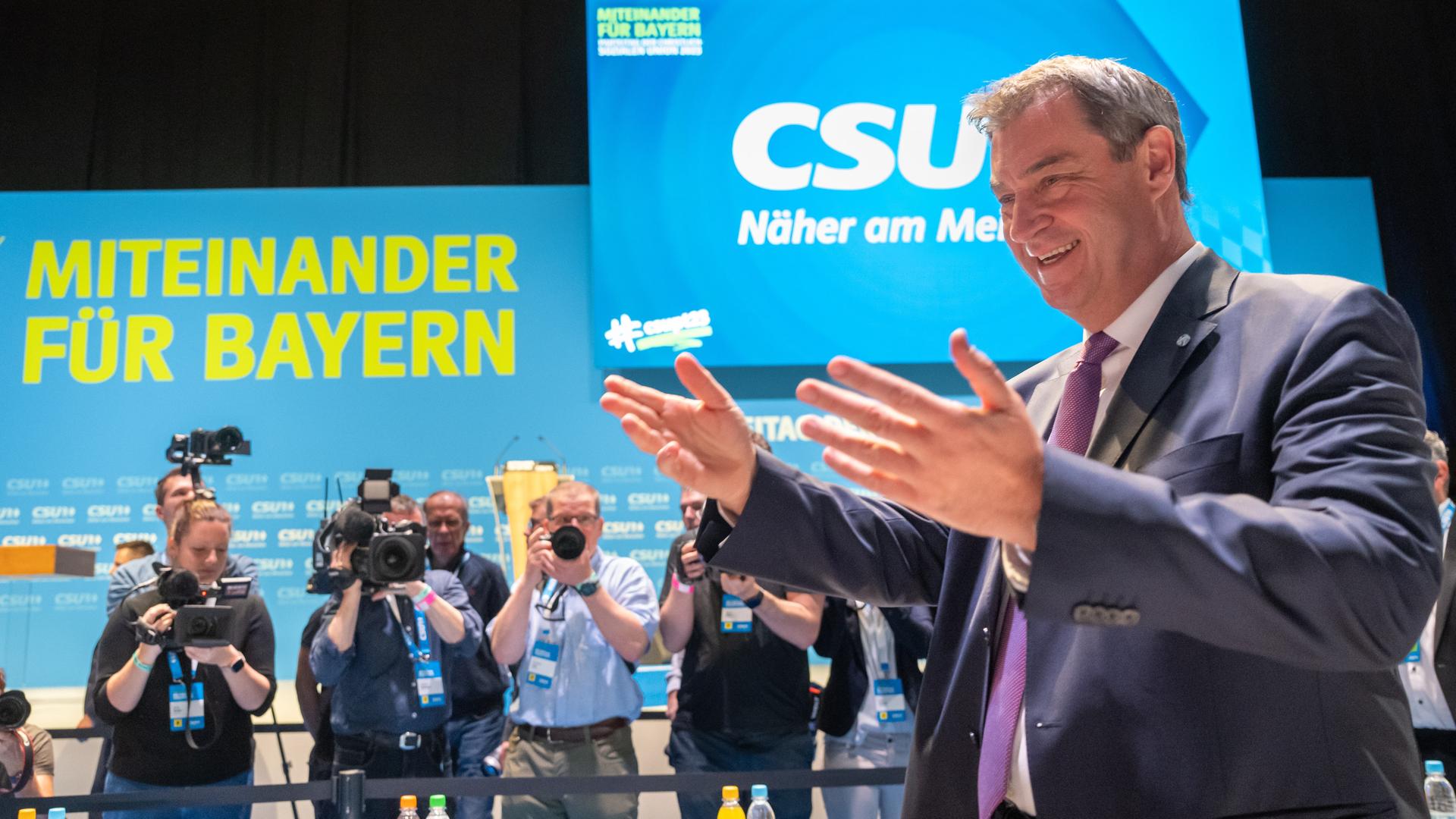 Markus Söder, Parteichef der CSU, auf dem CSU-Parteitag in Nürnberg. Er gestikuliert mit den Händen. Söder steht vor einem Bildschirm, auf dem steht: "CSU. Näher am Menschen". Hinter ihm sind Kameraleute zu sehen.