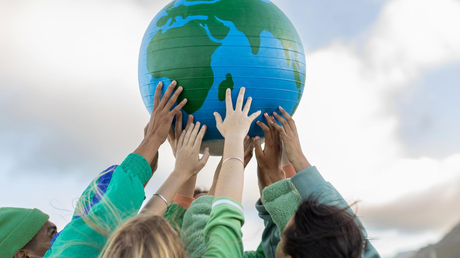 Eine Gruppe junger Menschen hält einen Globus in die Luft.