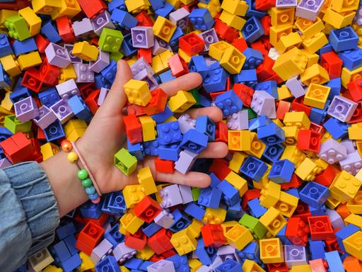 Ein Mädchen greift in eine Kiste voller Lego-Steine. 
