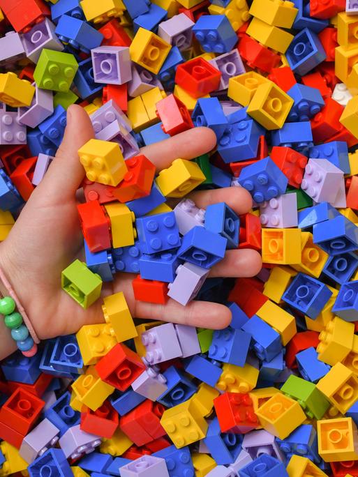 Ein Mädchen greift in eine Kiste voller Lego-Steine. 