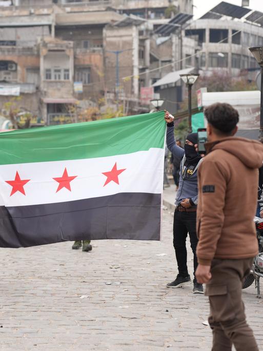 Junge Männer laufen mit aufgespannter syrischer Flagge durch die Stadt Hama