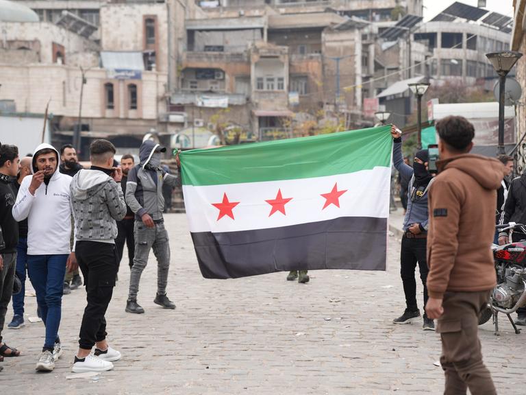 Junge Männer laufen mit aufgespannter syrischer Flagge durch die Stadt Hama