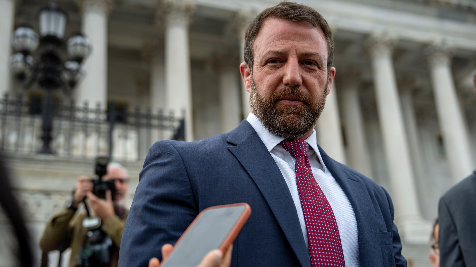 Markwayne Mullin steht vor dem Kapitol und spricht mit Reportern. Er schaut direkt in die Kamera.