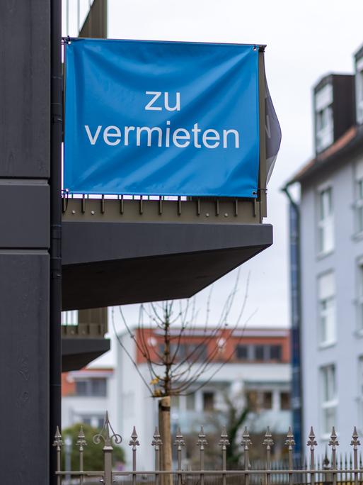 "Zu vermieten" steht auf einer Plane, die an einem Balkon-Geländer einer Neubau-Wohnung angebracht ist.