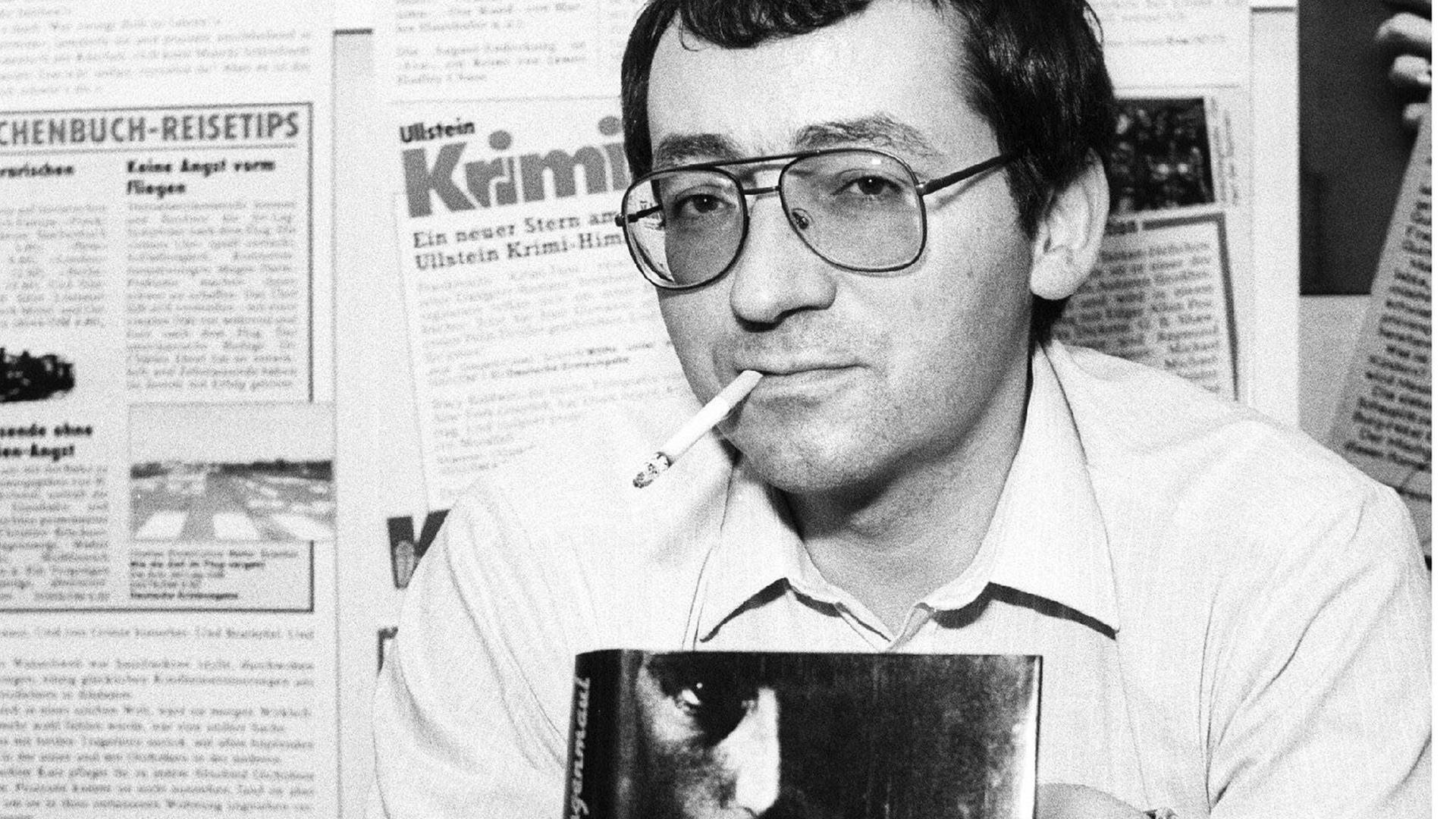 Schwarz-weißes Bild von Jörg Fauser während der Buchmesse 1985 in Frankfurt am Main, halb sitzend mit Buch und Zigarette im Mundwinkel rauchend