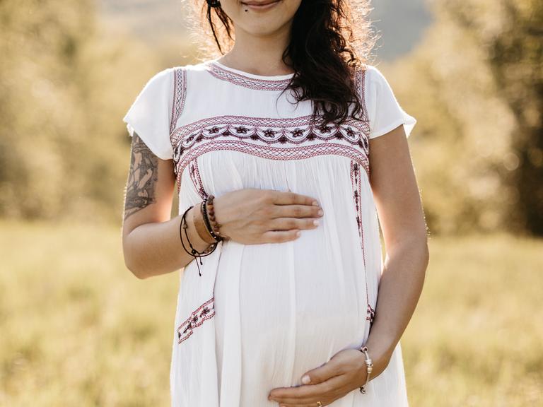 Das Hörspiel basiert auf einer wahren Begebenheit. 2014 wurden sieben Teenager in Bosnien und Herzegowina "kollektiv" schwanger. Zu sehen: Eine junge Frau (Gesicht erst ab den Lippen zu sehen) in einem weißen Kleid hält ihre Hände über den schwangeren Bauch. 