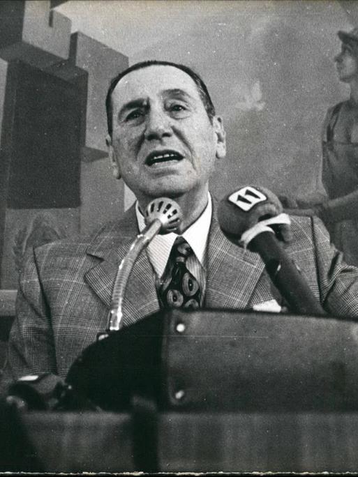 Juan Domingo Perón steht neben seiner Frau an einem Rednerpult und spricht engagiert ins Mikrofon