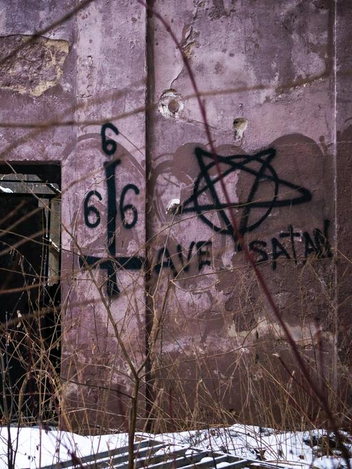 Eine altes, zerstörtes Gebäude. Auf die Wand wurden Pentagrame, verdrehte Kreuze und die Zahl 666 gemalt. Eine altes, zerstörtes Gebäude. Auf die Wand wurden Pentagrame, verdrehte Kreuze und die Zahl 666 gemalt.