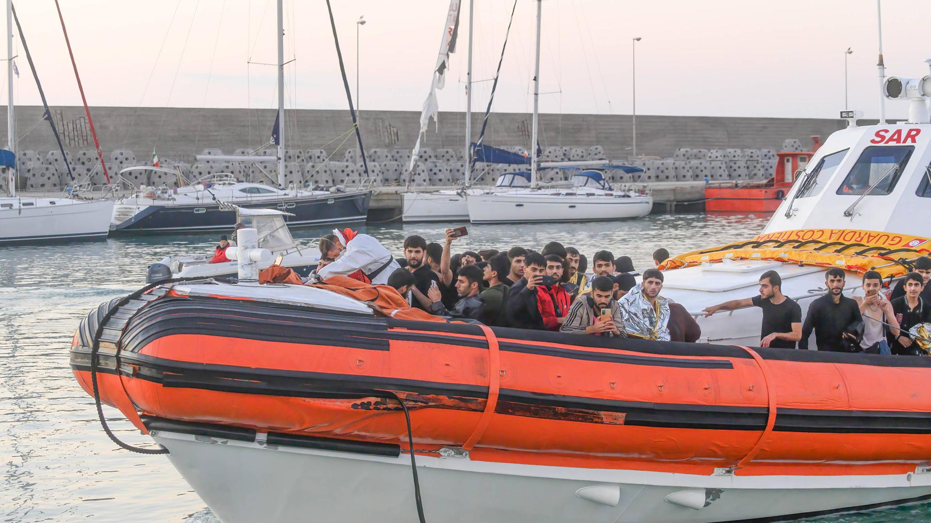 Flüchtlinge stehen auf einem Rettungsboot, das in einen Hafen an der italienischen Küste einfährt.