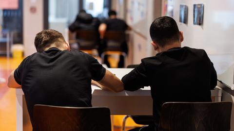 Schüler einer Realschule in München schreiben während einer Unterrichtsstunde in ihre Schulhefte.Man sieht sie von hinten mit schwarzen T-Shirts am Tisch sitzend. Schüler einer Realschule in München schreiben während einer Unterrichtsstunde in ihre Schulhefte.Man sieht sie von hinten mit schwarzen T-Shirts am Tisch sitzend.