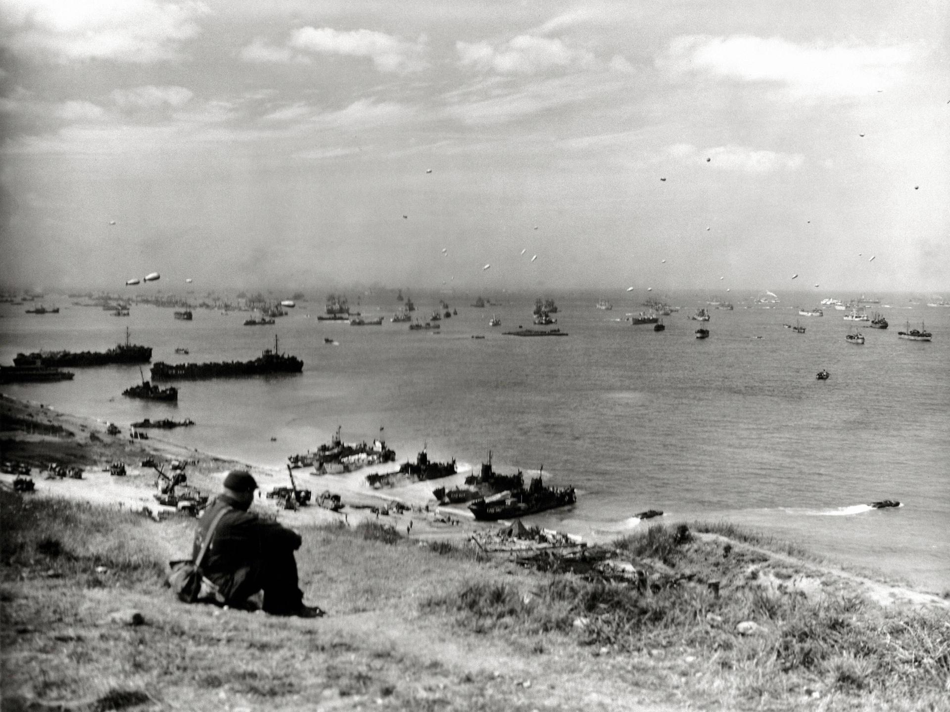 Ein Soldat beobachtet vom Strand aus die Landung von Kriegsschiffen in der Normandie.
