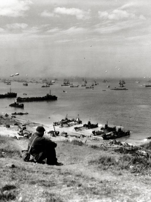 Ein Soldat beobachtet vom Strand aus die Landung von Kriegsschiffen in der Normandie.