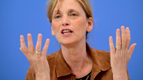 Karin Prien sitzt vor einem blauen Hintergrund und spricht gestikulierend.