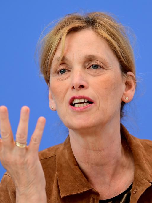 Karin Prien sitzt vor einem blauen Hintergrund und spricht gestikulierend.