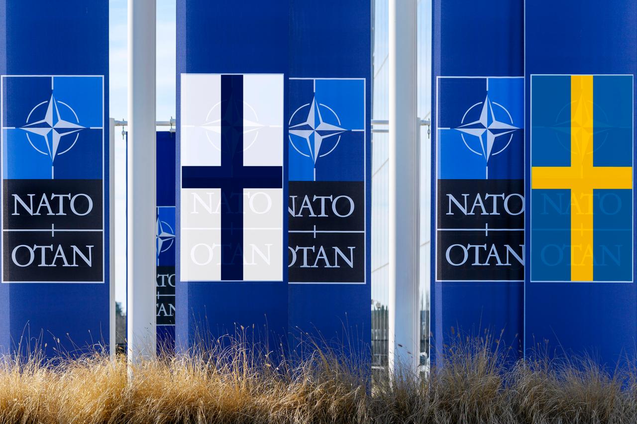 Die Symbole der NATO  mit den Fahnen Schwedens und Finnlands.