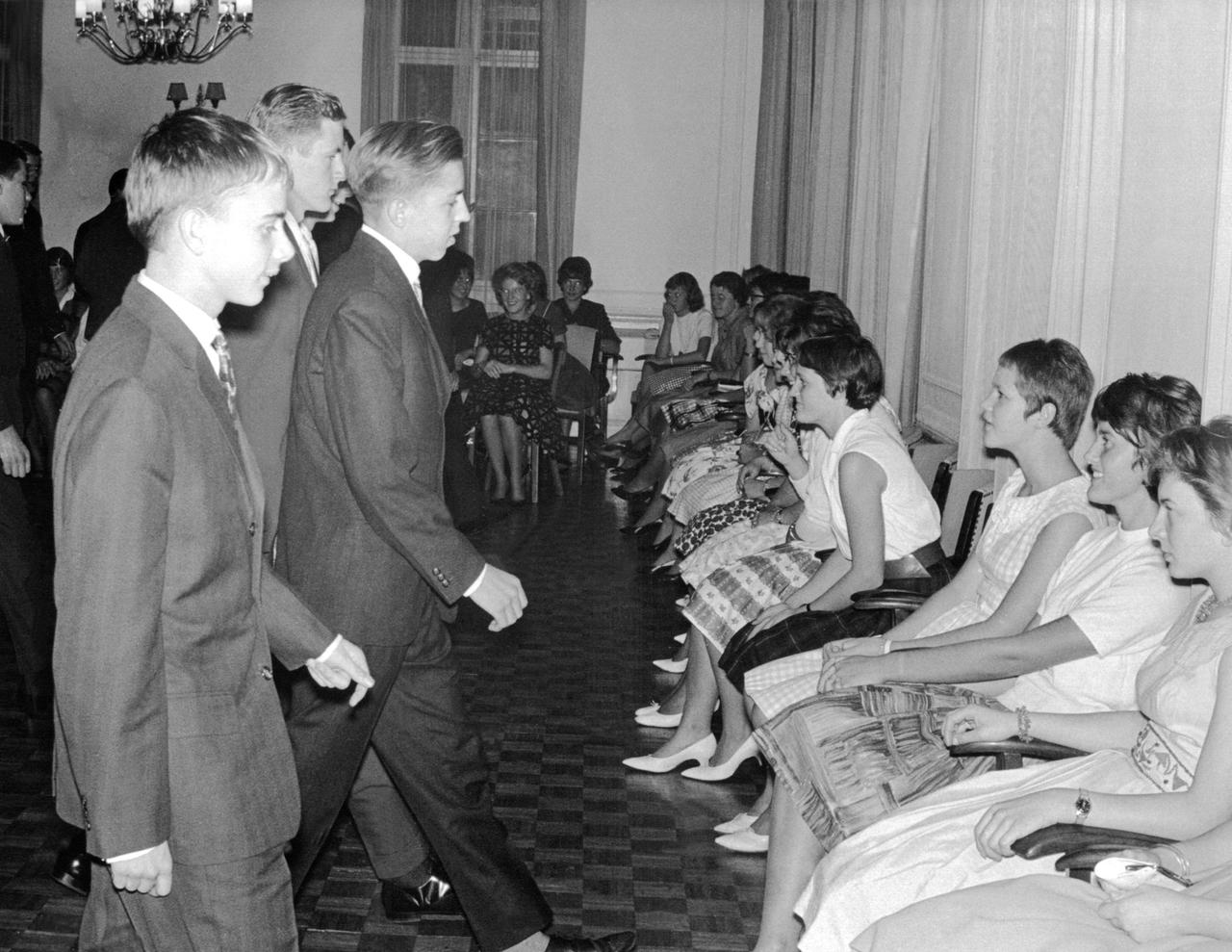 Schwarz-Weiß-Aufnahme einer Tanzstunde bei der die jungen Frauen sitzen und von den jungen Männern aufgefordert werden.