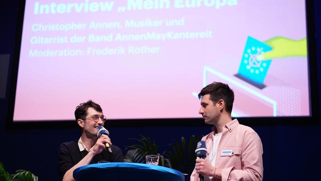 Zu sehen ist Gitarrist Christopher Annen im Gespräch mit Moderator Frederik Rother auf der Europakonferenz im Deutschlandfunk.