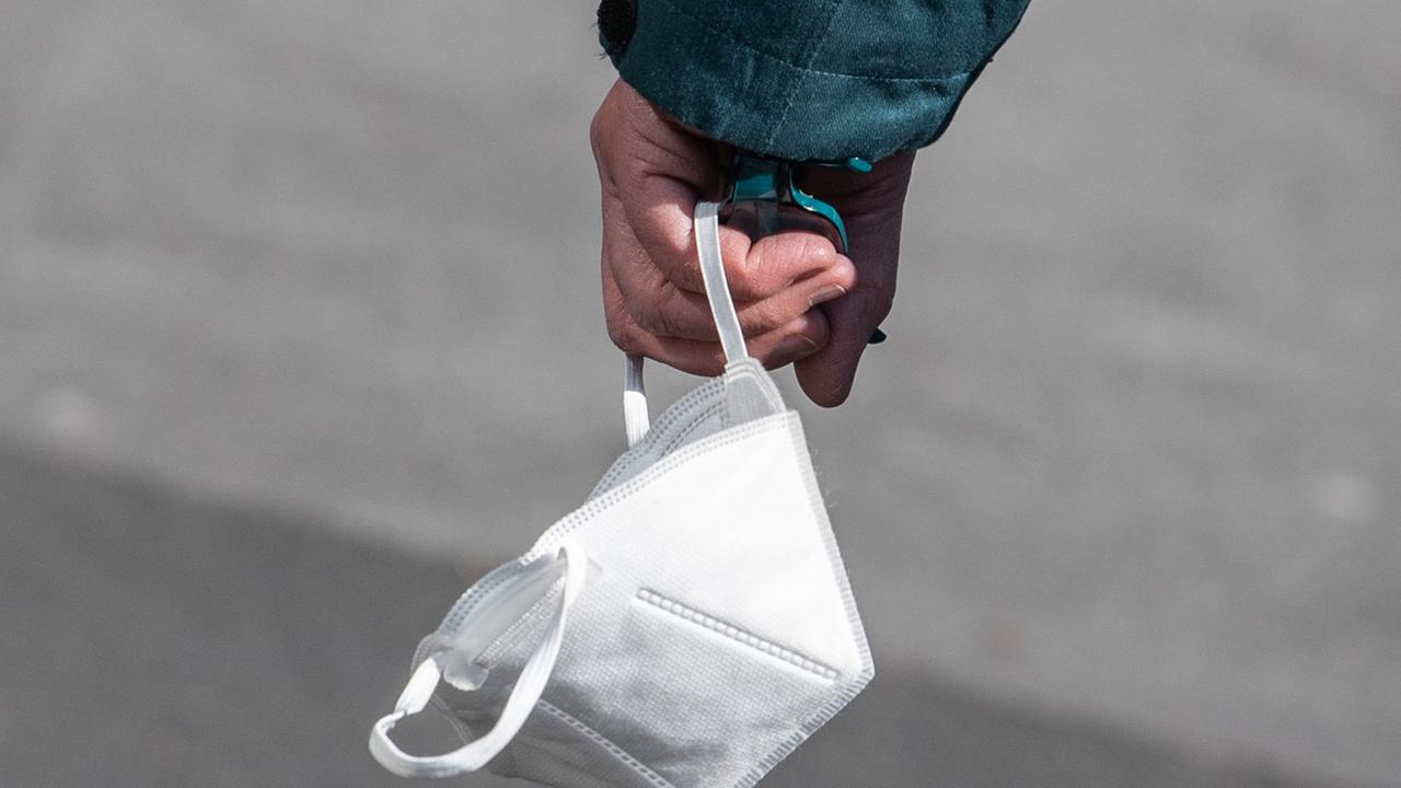 Eine Passantin trägt in einer Fußgängerzone ihre FFP-2 Maske in der Hand. Eine Passantin trägt in einer Fußgängerzone ihre FFP-2 Maske in der Hand.