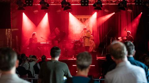 Konzert von Max Herre & Roberto di Gioia live auf dem Jazz in the City Festivals im Zughafen Erfurt. Man sieht die Zuschauer, die auf die Bühne blicken. Auf der Bühne stehen in rotes Licht getaucht die Musiker.