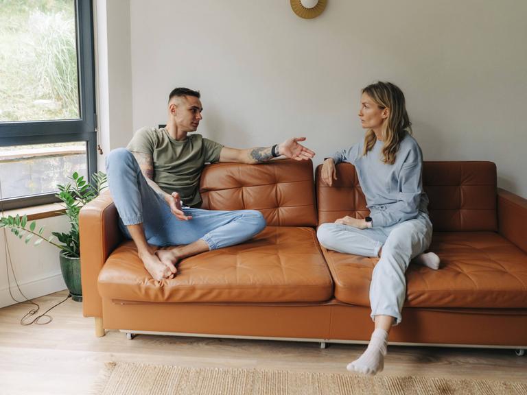 Ein Mann und eine Frau diskutieren auf einer Couch Ein Mann und eine Frau diskutieren auf einer Couch
