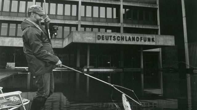 Schwarz-Weiß-Aufnahme eines Mannes, der vor dem Funkhaus des Deutschlandfunk in Köln eine Angel ins Wasser hält
