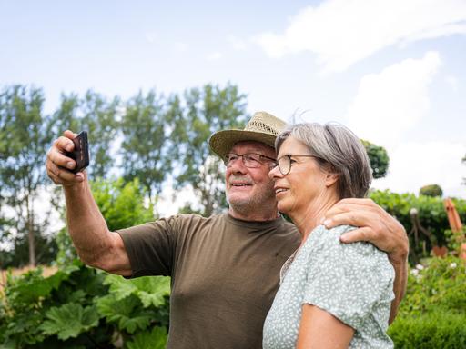 Ein älteres Pärchen macht mit dem Smartphone Selfies im Garten (gestellte Szene).
