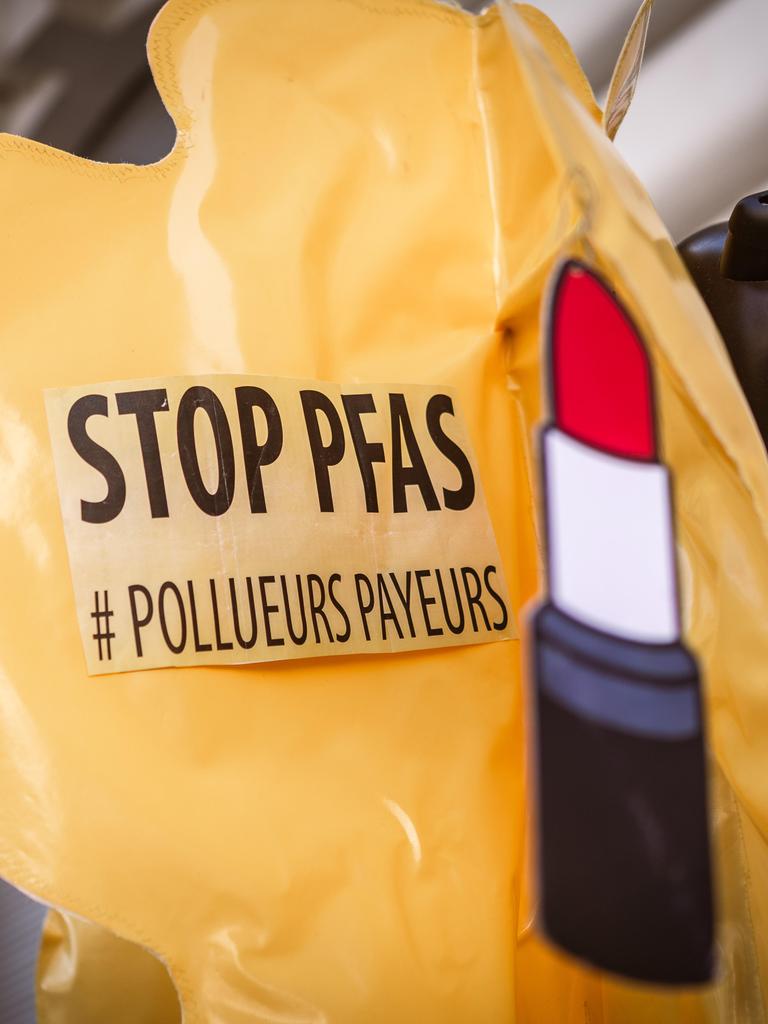 Ein Aufkleber mit der Aufschrift "Stop PFAS" und einer Abbildung eines Lippenstifts sind auf einem aufblasbaren, gelben Plastikballon befestigt.