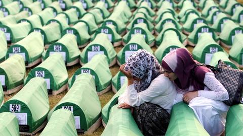 Zwei Frauen trauern während der Beerdigung von neu identifizierten bosnischen Muslimen in Srebrenica 2010. Sie sitzen zwischen hunderten nummerierten Särgen, die mit grünem Stoff bespannt sind.